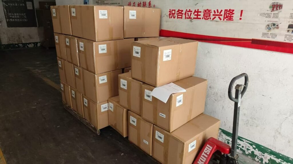 Cartons stacked by a warehouse door with a pallet jack